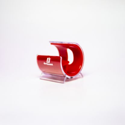 A small, plastic cellphone holder with a red interior and clear exterior, featuring the Holidynamics logo on the front. The holder is shaped like a curved “C” and sits on a white background.