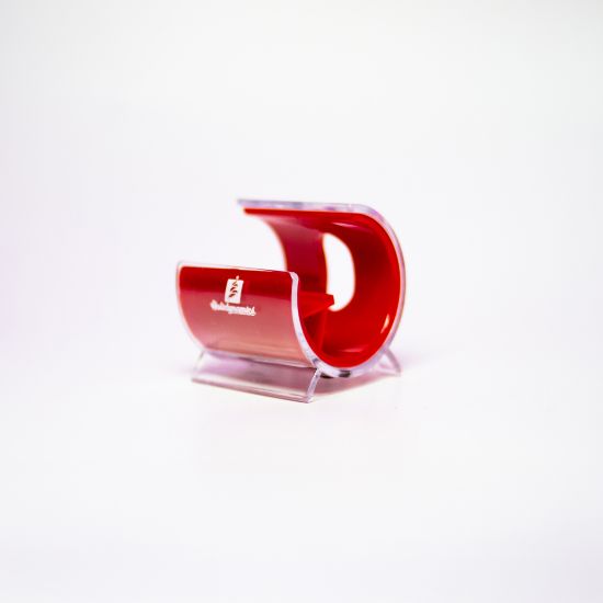 A small, plastic cellphone holder with a red interior and clear exterior, featuring the Holidynamics logo on the front. The holder is shaped like a curved “C” and sits on a white background.
